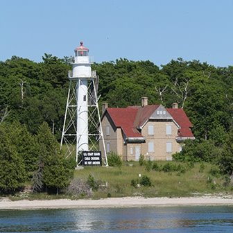 A lighthouse next to a building surrounded by trees.