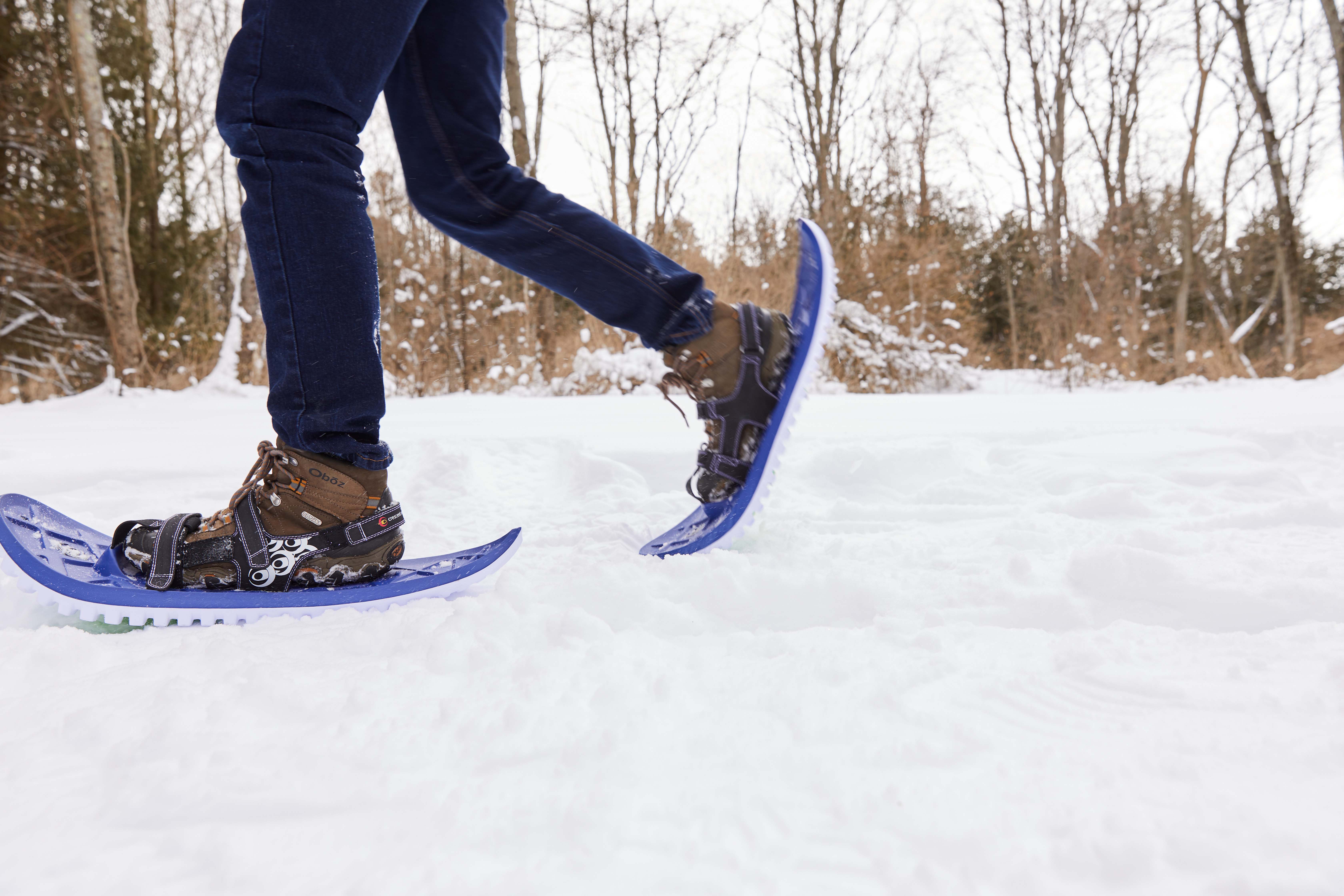 A closeup of someone snowshoeing in a wooded clearing