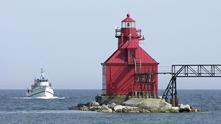 Red lighthouse on a rocky outcropping with a boat coming in.