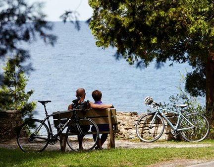 Cyclist couple sitting on a bench looking out at the lake.