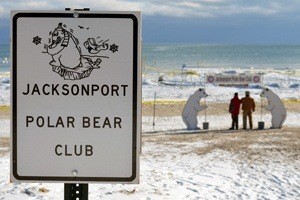 A sign that says "Jacksonport Polar Bear Club" with two people standing between two polar bear statues in the distance.