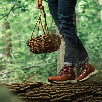 A closeup of a person in hiking boots and carrying a basket standing on a log