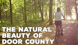 A person biking down a wooded path with a text overlay that says "The Natural Beauty of Door County"