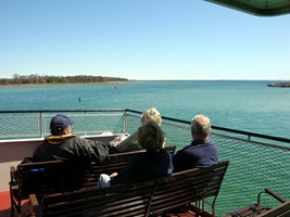 A group sits on a ferry deck and admires a blue-green lake and wide-open horizon