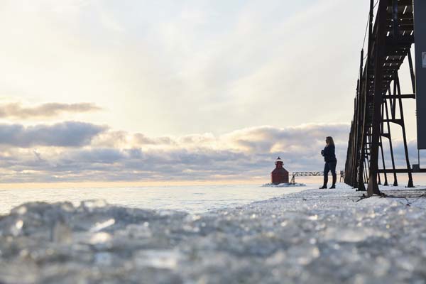 A woman stands at an icy pierhead during sunrise.