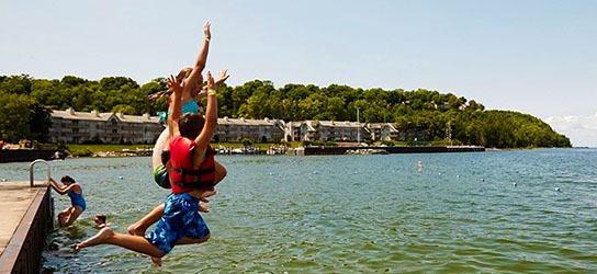 Kids jumping off of a dock into the lake.