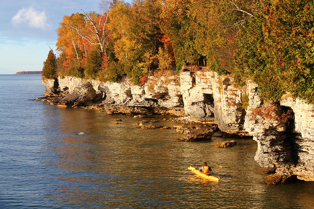 Kayaker paddling next to stone face with autumnal trees