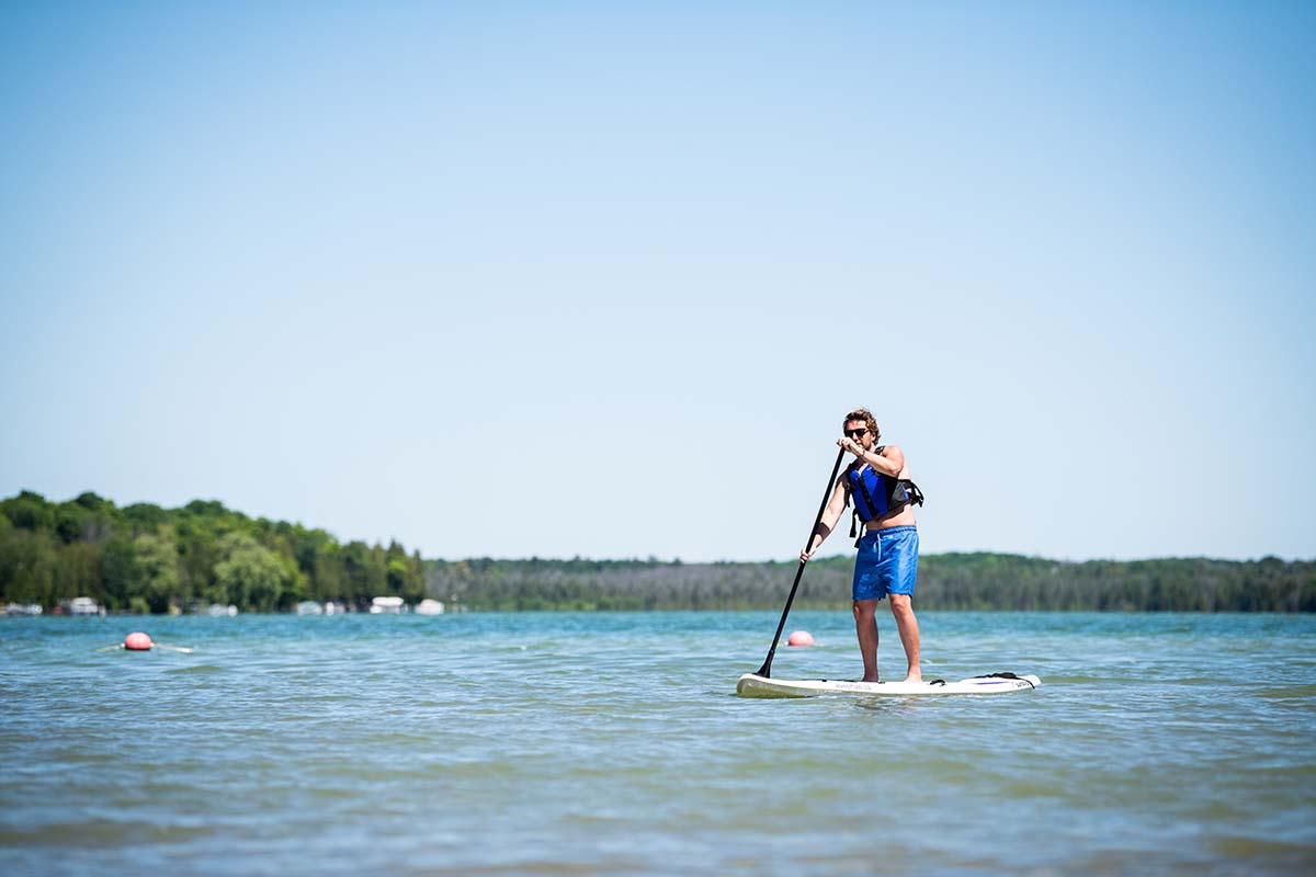A man paddle boards across a crystal-blue lake.