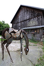 A metal sculpture of a horse in front of a barn.