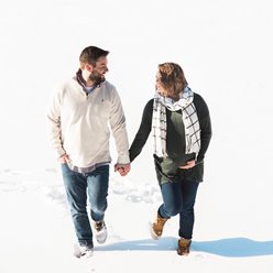 A couple walking in the snow holding hands and smiling at each other