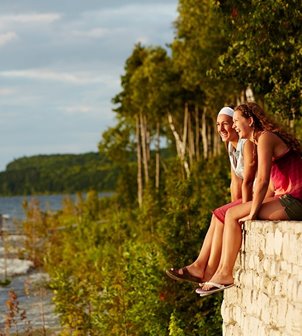 Two women sitting on a stone wall laughing and looking out on the lake.
