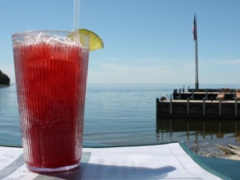 A cherry juice margarita sits on table beside the lake.