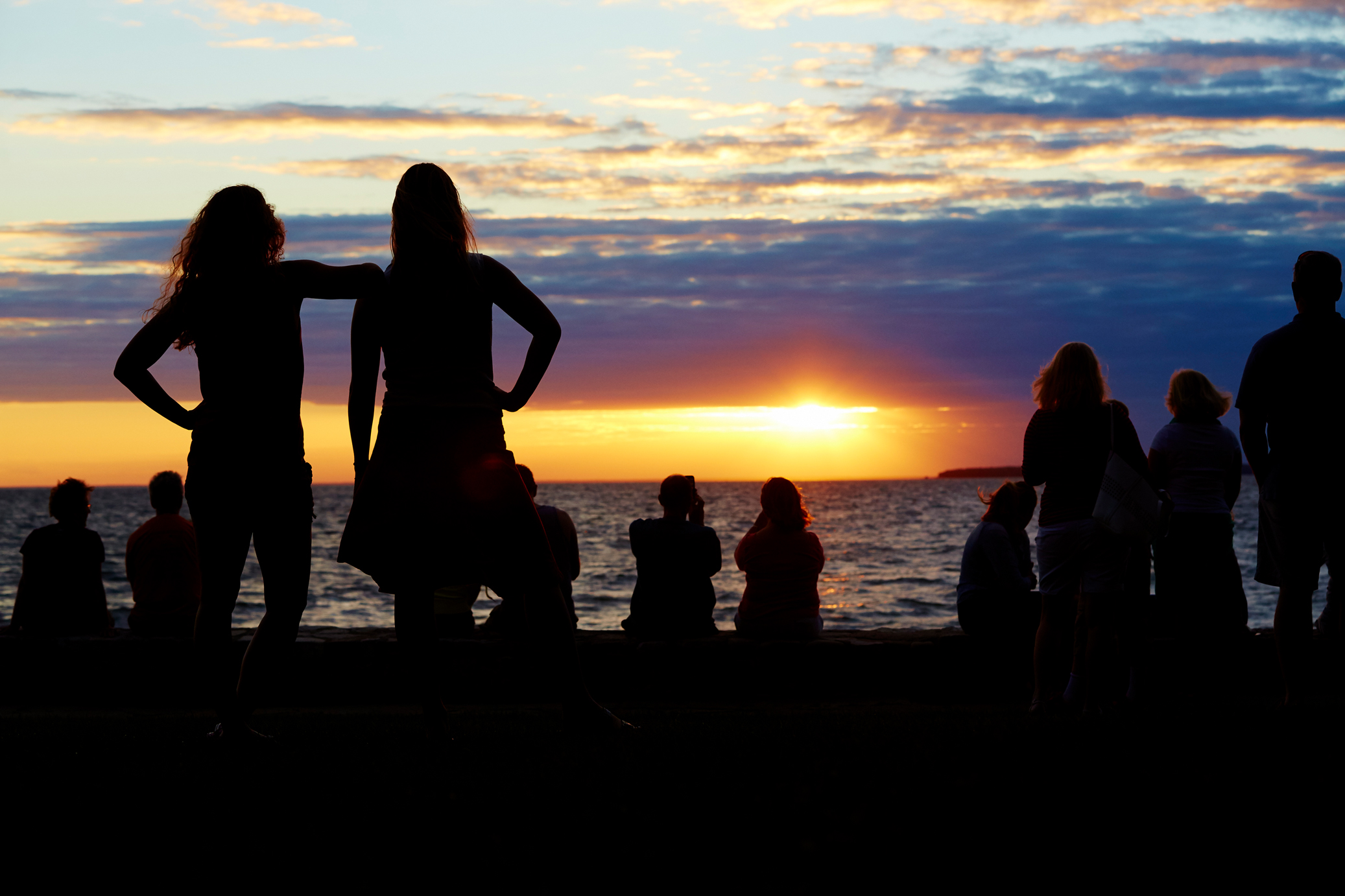 A group of people silhouetted against a gold and purple sunset.