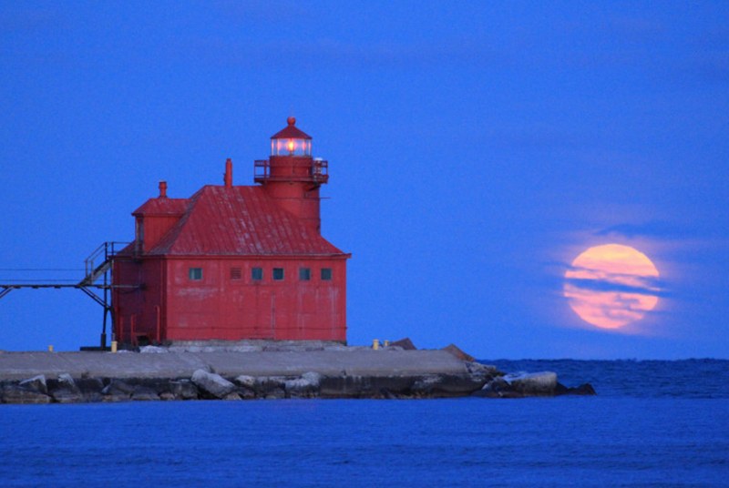 Red lighthouse on a rocky outcropping with the full moon low in the sky