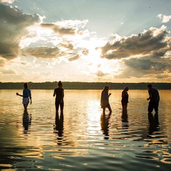 A group of people standing in the lake silhouetted by the sunset