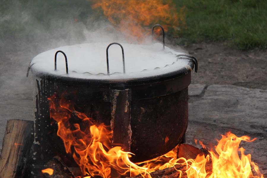 A kettle of fish nearly boils over atop a firepit.