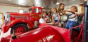 Family playing on fire truck in a museum.