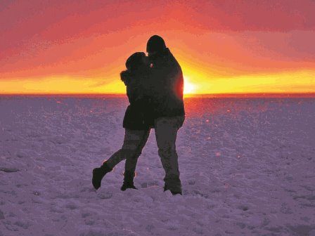 A couple standing in the snow hugging at sunset.