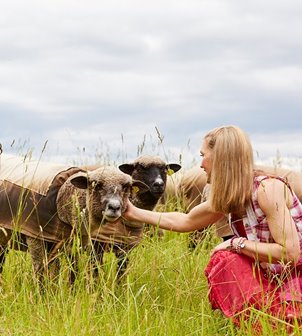 A woman bent down in the grass petting sheep.