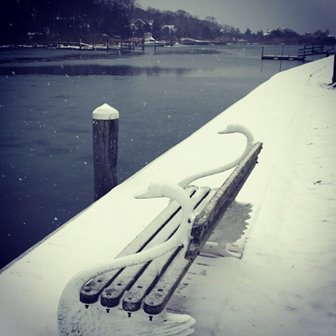 A bench decorated with swans on a snow-covered dock.