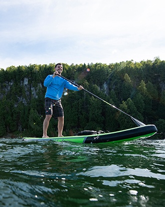 A man paddle boards past a massive limestone wall, part of the Niagara Escarpment.