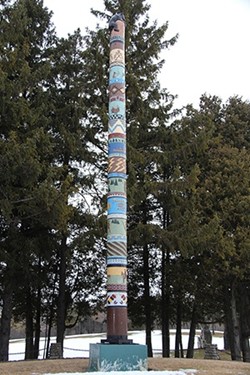 A totem pole standing in front of trees.