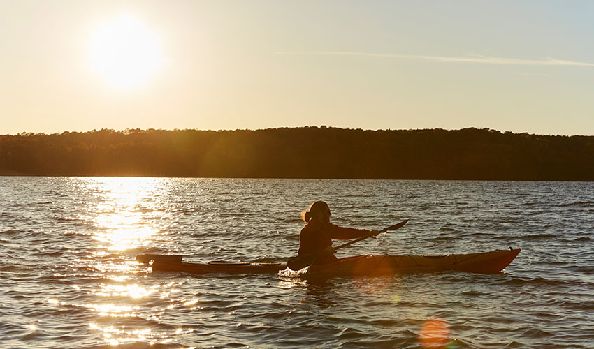 A woman paddles a kayak on an inland lake at sunset