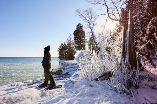 A woman snowshoeing and enjoying the view at Cave Point.