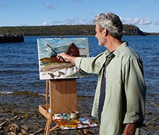 Man painting a barn by the lake.
