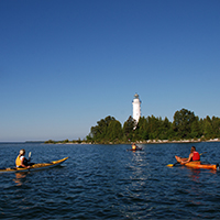 Kayaks on the lake with a lighthouse in the distance.