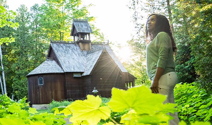 A woman immersed in nature and sunlight near a wooden building.