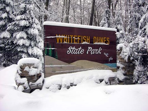 A snow-covered sign at Whitefish Dunes State Park.