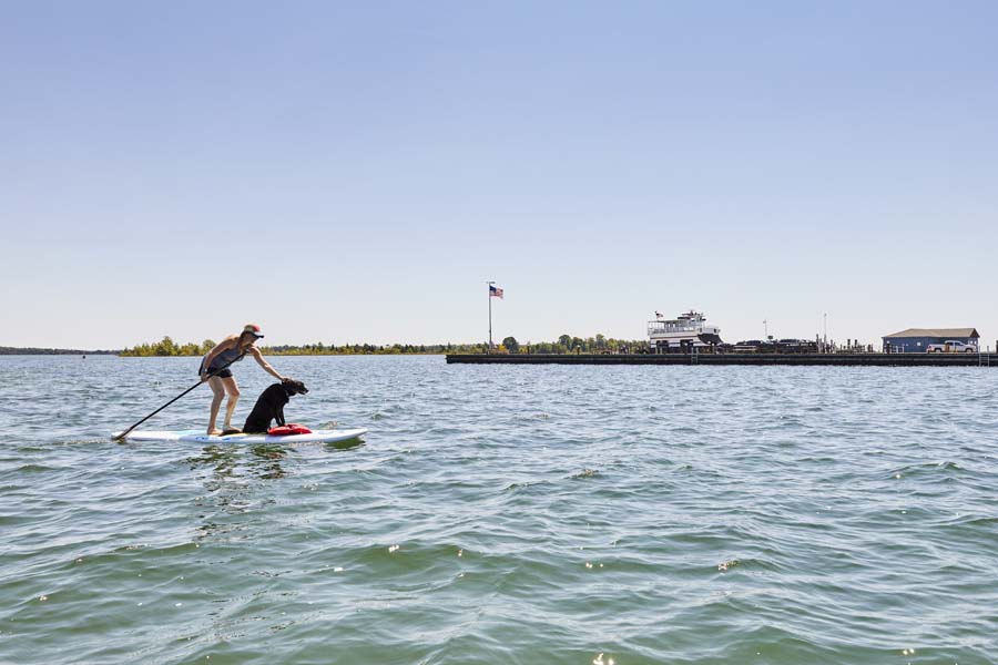 A woman paddle boards with her dog aboard.