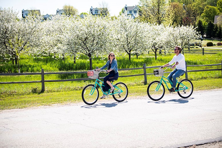 Two people biking past blossoming trees.