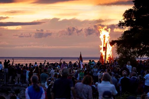 A large fire burns at sunset as Fyr Bal revelers look on.