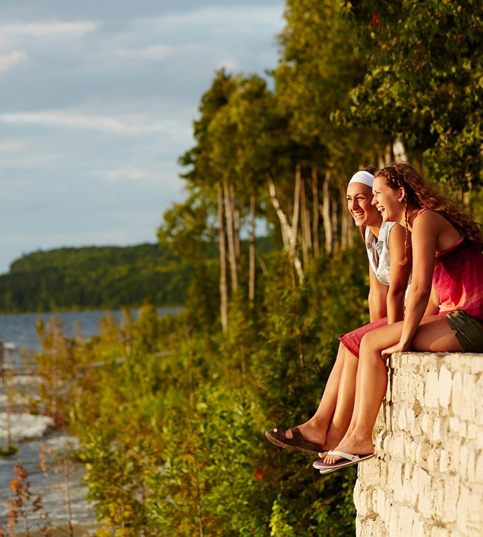 Two women sitting on a wall ledge looking out at the water.