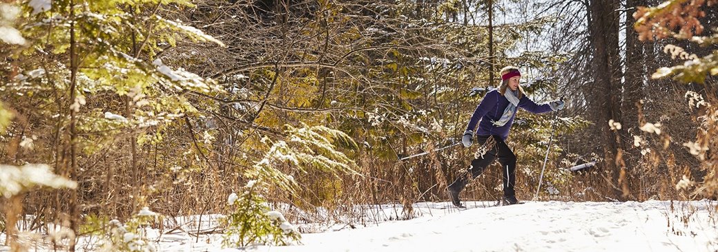 A woman cross country skiing through the woods.