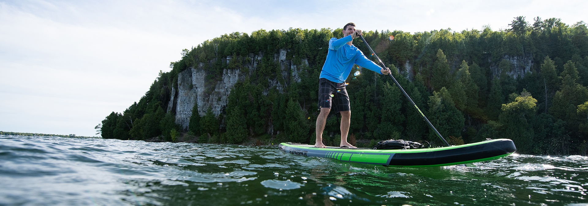 A man paddle boards on the lake with the bluffs of the Niagara Escarpment behind him