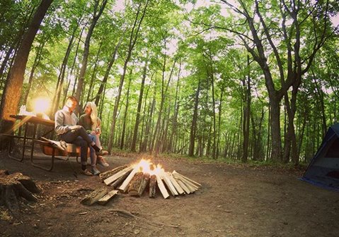 A couple sitting at a picnic table by a campfire.