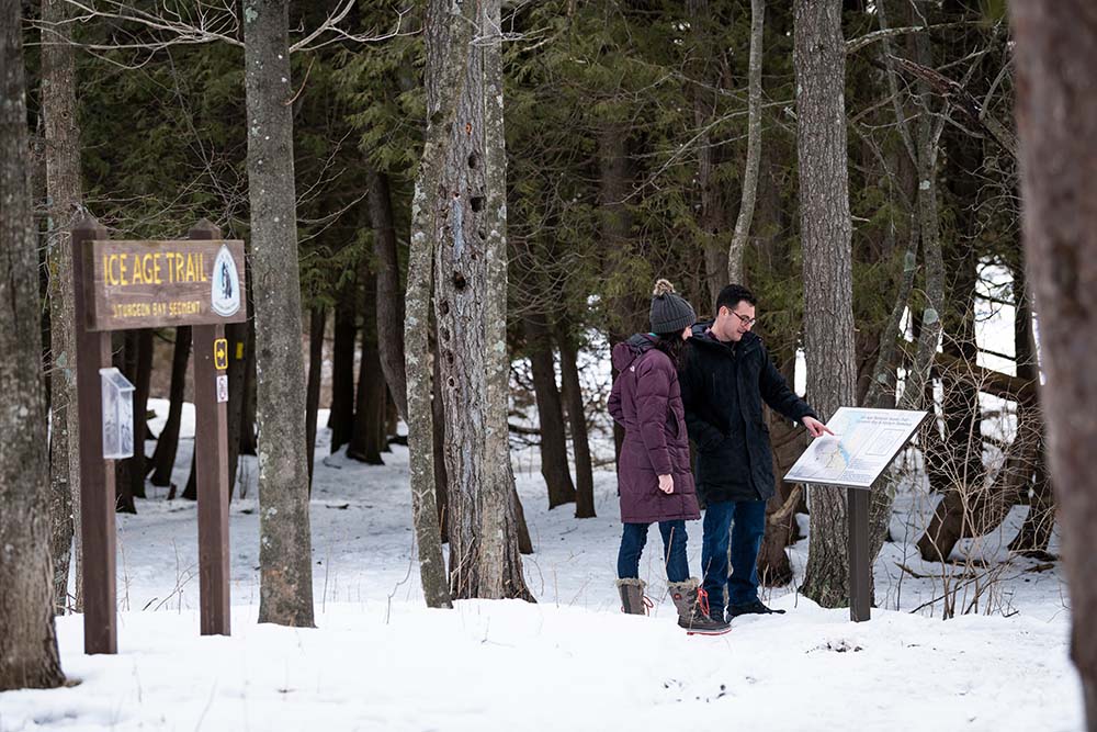 A couple looking at a sign in the woods with snow on the ground