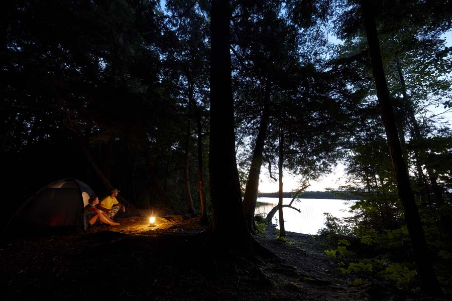 A couple site by a campfire at a remote lakeside campsite at night.