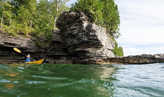 A kayaker on the lake below tree-lined cliffs.