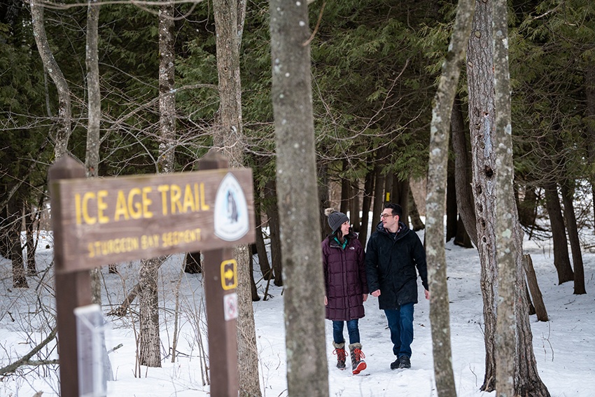 A couples walks through the trees on a snowy section of the Ice Age Trail
