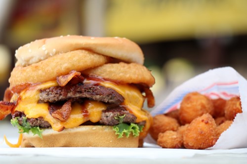 A juicy cheeseburger topped with bacon and onion rings accompanied by fried cheese curds.