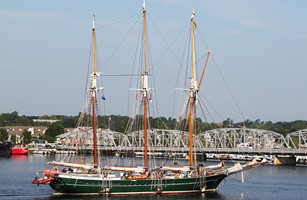 Tall sailing ship in front of a steel bridge.