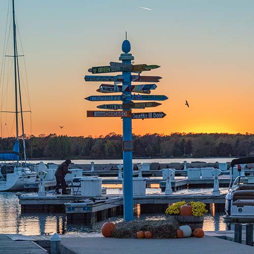 Sign post and marina with a sunset in the background.