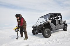 A man drilling an ice fishing hole next to an ATV