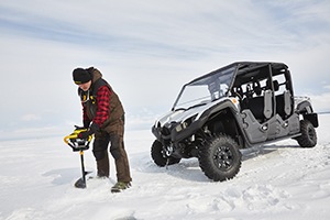 A man drilling an ice fishing hole next to an ATV
