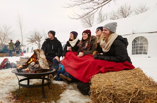A group of friends sit around an outdoor fire at Winter Fest.