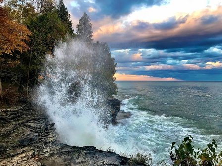 Water crashing up on rocky cliff side with fall trees in the background